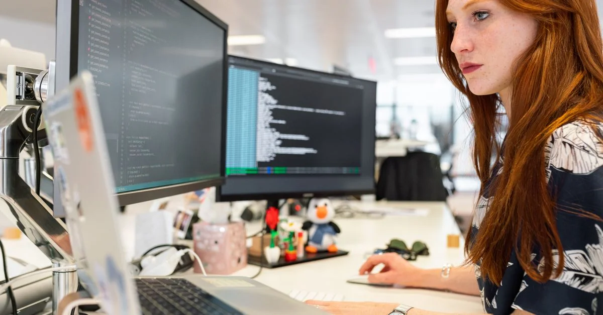 Une ingénieure logicielle concentrée codant sur des écrans doubles dans un bureau moderne.