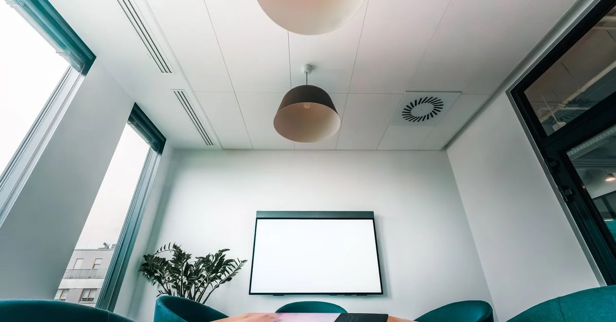 Salle de conférence spacieuse et lumineuse avec un écran vide, idéale pour des présentations ou des réunions.
