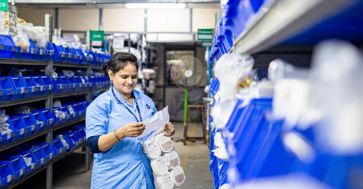 Une femme en uniforme bleu organise l'inventaire dans une allée d'entrepôt, axée sur l'efficacité.