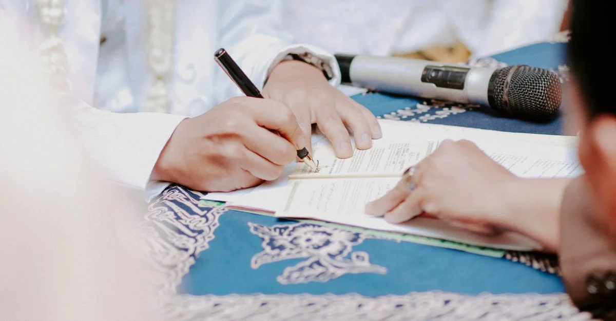 Gros plan sur des mains signant des documents de mariage avec un microphone sur la table.