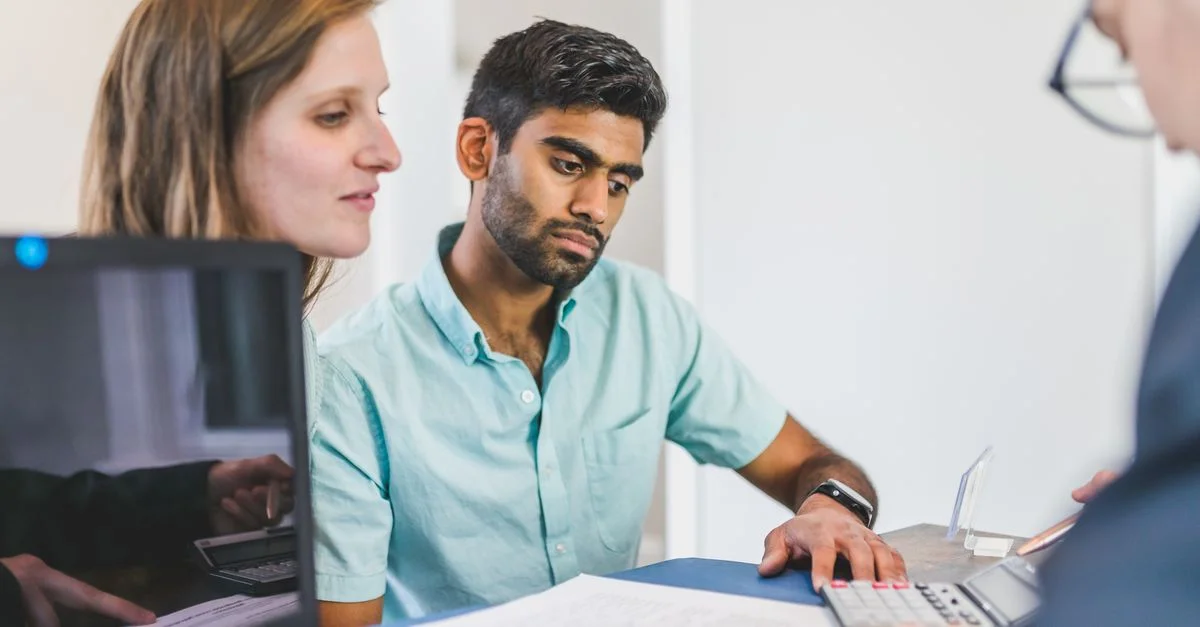 Un jeune couple en discussion avec un agent immobilier dans un cadre de bureau moderne.