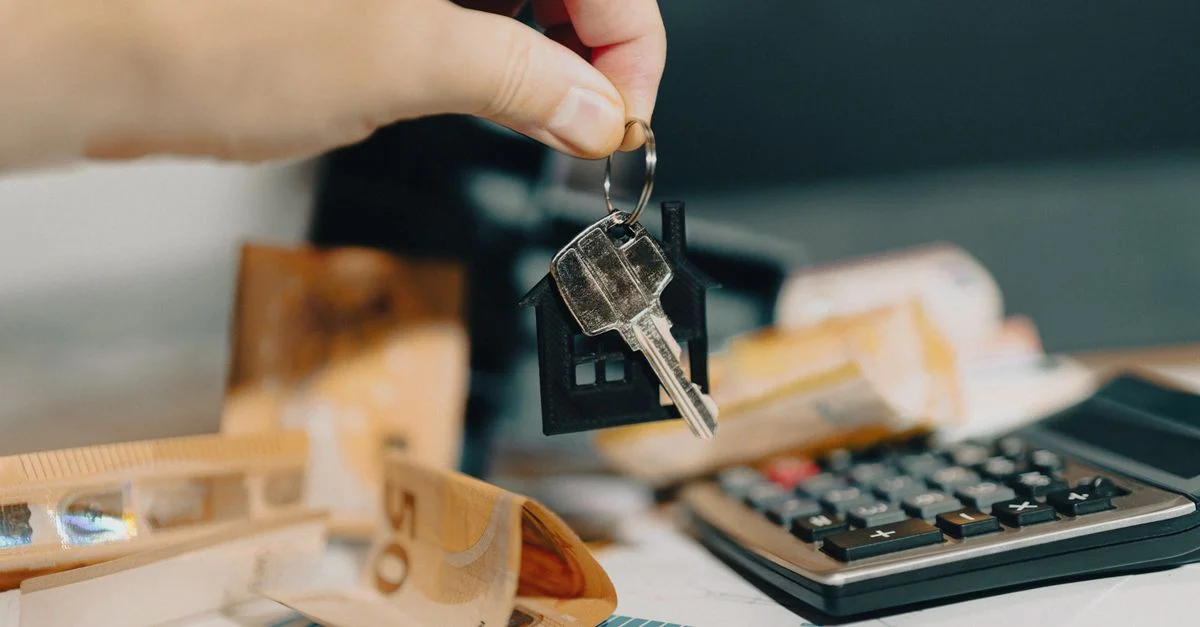 Gros plan sur une main tenant des clés au-dessus d'euros et d'une calculatrice, symbolisant l'achat immobilier.