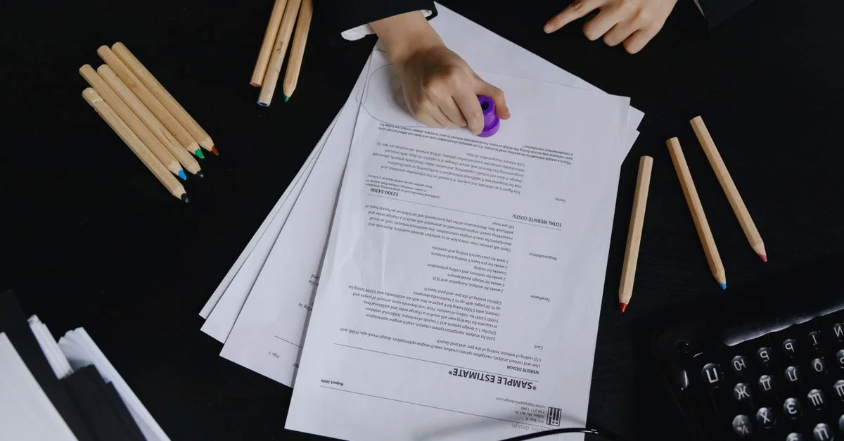 Mains travaillant avec des documents et des crayons de couleur sur un bureau noir.