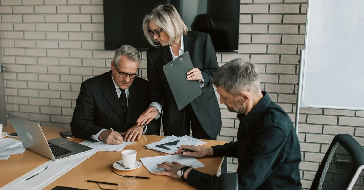Trois professionnels matures en réunion d'affaires discutent et signent des documents dans un bureau.