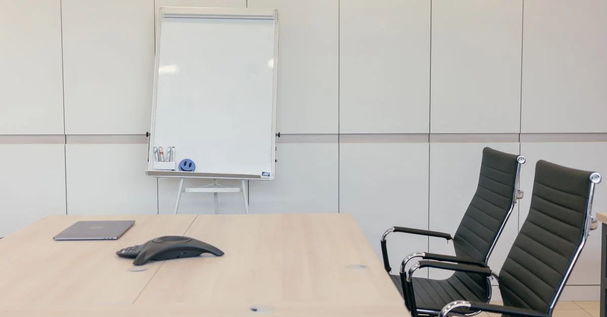 Salle de conférence élégante avec des chaises, une table et un tableau blanc prêts pour une réunion.