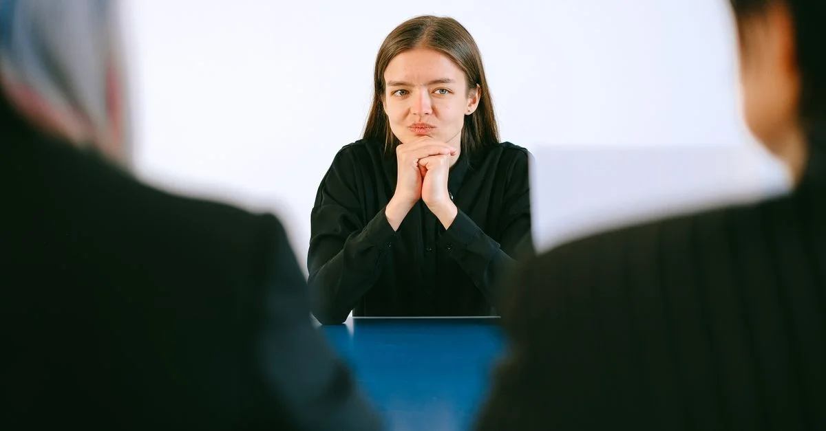 Une femme lors d'un entretien d'embauche face à deux personnes autour d'une table de bureau, se concentrant intensément.