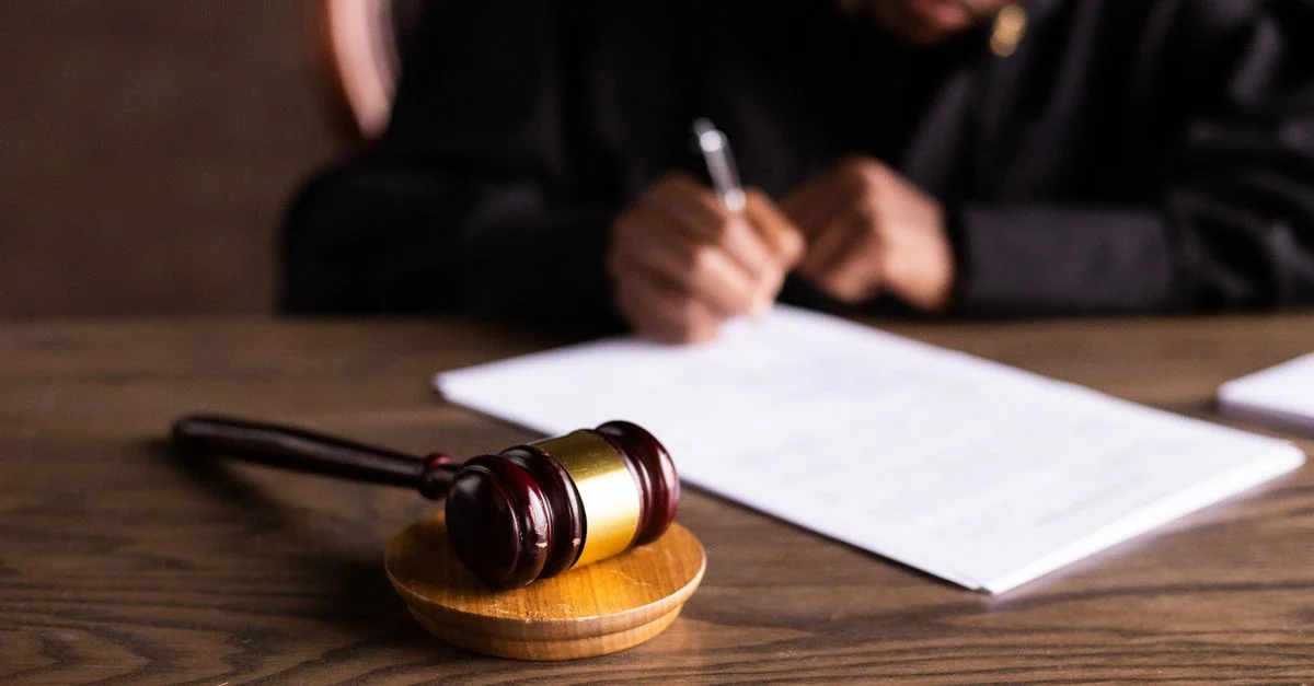 Juge signant des documents sur un bureau avec un accent sur le maillet, représentant la loi et la justice.