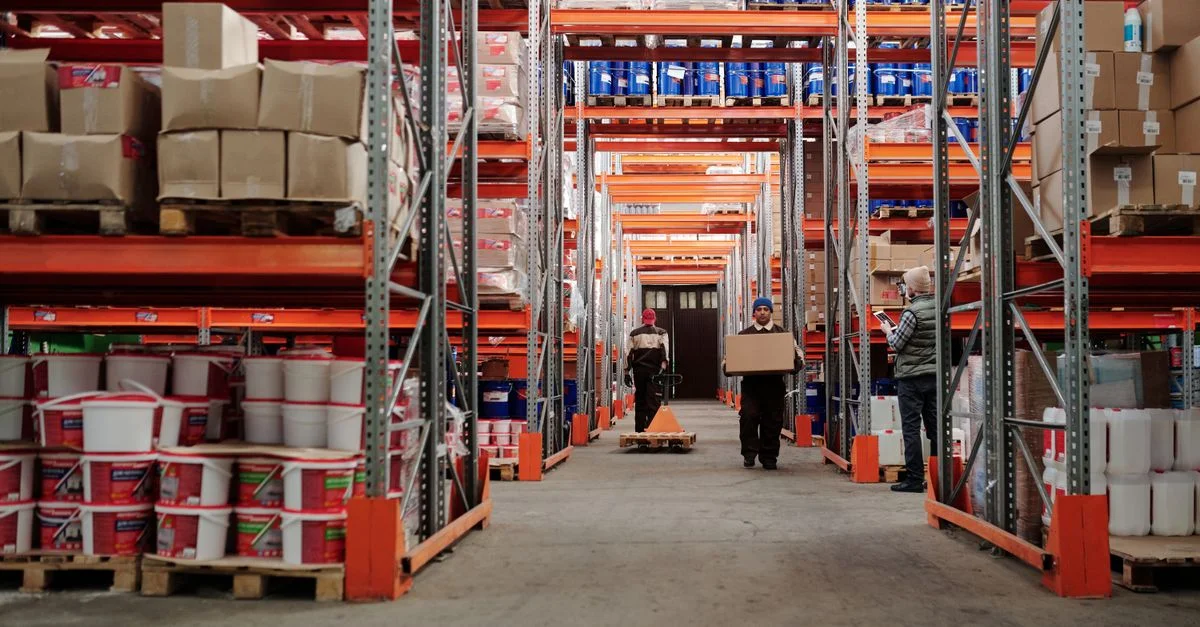 Intérieur d'un entrepôt montrant des travailleurs manipulant des cartons et des étagères organisées remplies de produits.