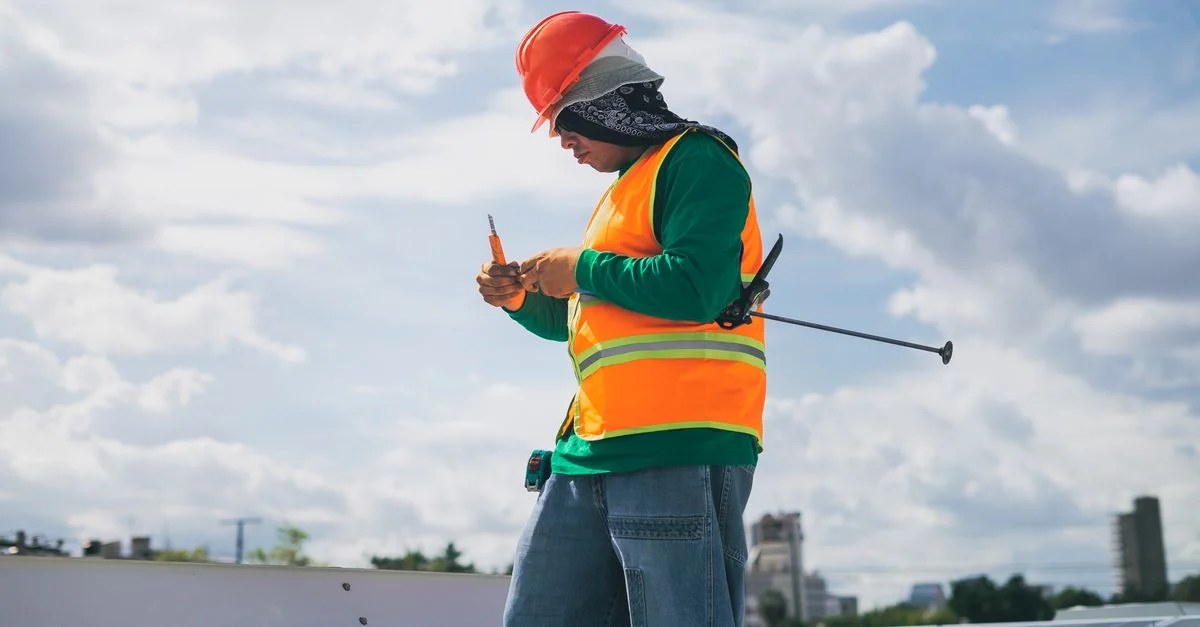 Un technicien solaire en équipement de protection travaille sur un toit sous un ciel bleu.