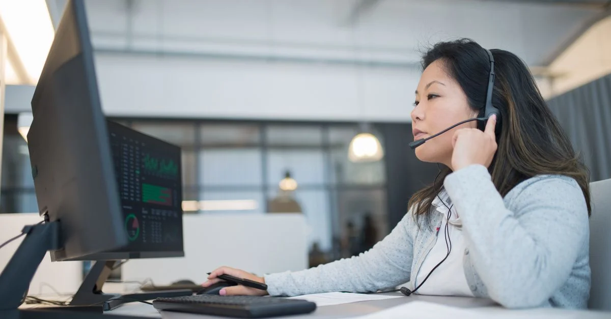 Une jeune femme asiatique portant un casque, travaillant au support client à un bureau moderne.