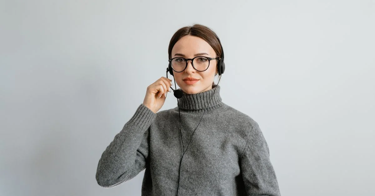 Femme caucasienne en pull gris et lunettes fournissant un support client avec un casque dans un bureau.